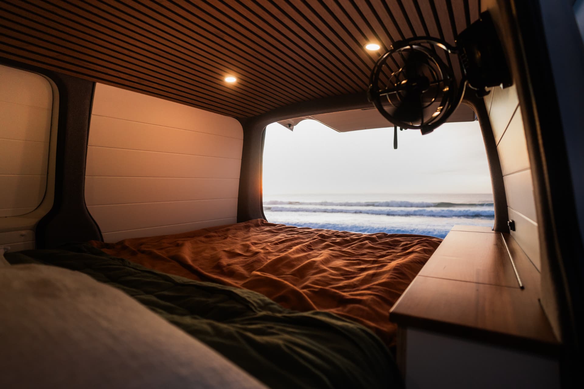 VW Transporter — Bed made up under the slatted oak ceiling, doors open to the surf